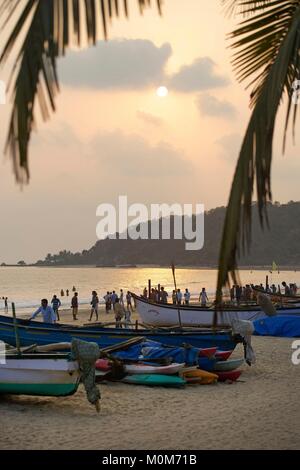 Indien, Goa, Palolem, Touristen in der goldenen Sand Strand mit Kokospalmen gesäumt, vor der Fischer Boote, bei Sonnenuntergang Stockfoto