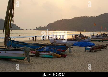 Indien, Goa, Palolem, Touristen in der goldenen Sand Strand mit Kokospalmen gesäumt, vor der Fischer Boote, bei Sonnenuntergang Stockfoto