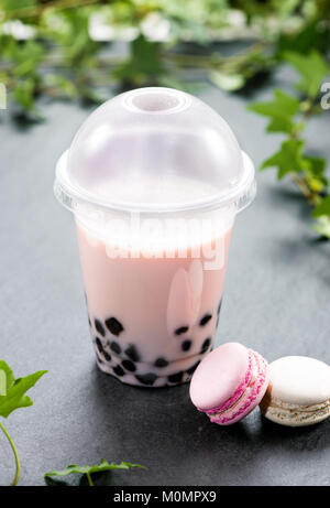 Hausgemachte Milch Bubble Tea und Tapioka Perlen in Schale aus Kunststoff mit Macarons auf Tisch. Stockfoto