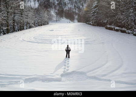 Jungen Erwachsenen aktiven Mann entfernt im malerischen Bergblick mit Schneeschuhen auf verschneiten Pfad in sonnigen Wintertag bei Sonnenaufgang im Freien. Stockfoto