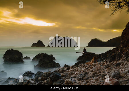 Frau mit Hut sitzen am Strand Stockfoto