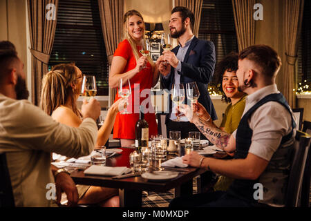 Freunde sind in der feierlichen Mahlzeit zusammen. Ein paar sind gemeinsam am Ende der Tabelle, wodurch ein Toast, zu dem jeder seine Glas angehoben wird Stockfoto