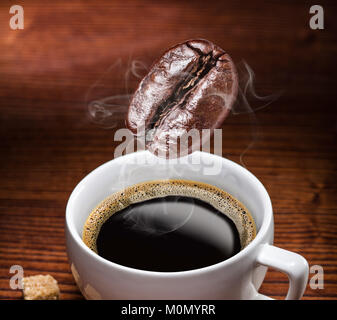 Gerösteter Kaffee Bohne in die Tasse Kaffee fallen. Konzeptionelle Bild. Stockfoto