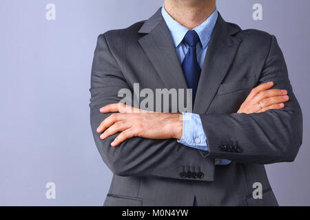 Junge Unternehmer stehen mit Waffen auf grauem Hintergrund gekreuzt Stockfoto