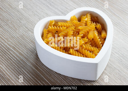 Trockene organische Glutenfreie fusilli Pasta in Herzform Schüssel auf hölzernen Tisch Stockfoto