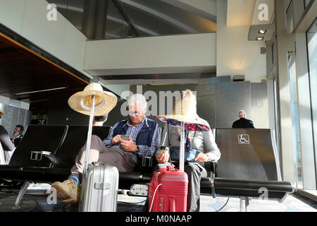 Ein älteres Ehepaar, das mit Gepäck und Strohhüten in den Urlaub fährt, sitzt in der Abfluglounge am Flughafen Los Angeles, Kalifornien, USA KATHY DEWITT Stockfoto