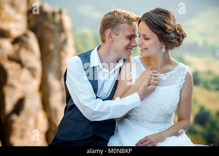 Emotionale Hochzeit portrait. Schöne junge jungvermählte Paar hübsches Lächeln, zärtlich, Hände und Nase zu reiben, während er auf den Felsen. Stockfoto