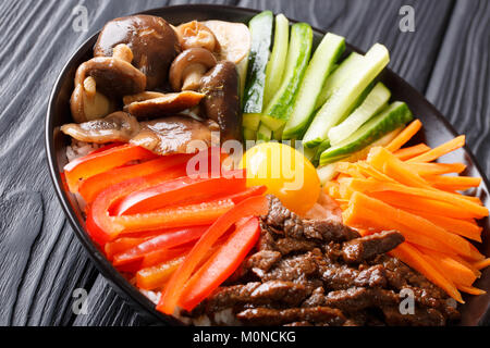 Koreanisches Essen Bibimbap mit gebratenem Rindfleisch, rohes Ei, Gemüse, Shiitake und Reis close-up in einer Schüssel auf dem Tisch. Horizontale Stockfoto