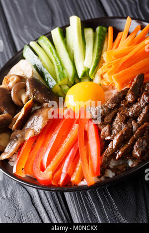 Leckeres koreanisches Essen Bibimbap mit Rindfleisch, Eigelb, Gemüse, Pilze und Reis close-up in einer Schüssel auf dem Tisch. Vertikale Stockfoto