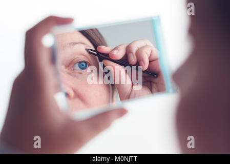 Frau Zupfen der Augenbrauen mit Pinzette durch die Fenster, selektiver Fokus Stockfoto