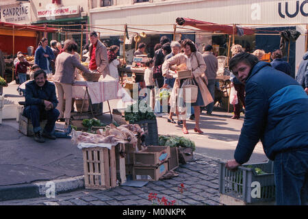 Frankreich, Quimper - Juli 1986: Leute wandern durch eine Straße Markt in Quimpier, Frankreich auf einem hellen Sommertag. Zwei Händler schauen direkt in die Kamera. Stockfoto