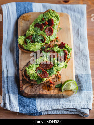 Avocado auf Toast mit Chorizo, Limette und Koriander. Auf einem Holzbrett serviert. Stockfoto
