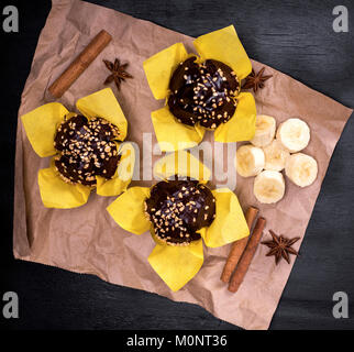 Chocolate Muffins mit einer Banane in gelbes Papier auf einem schwarzen Hintergrund gewickelt, Ansicht von oben Stockfoto
