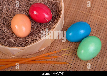 Bunte Eier im Stroh in einem Korb und Kerzen auf einer Matte nächste Stockfoto