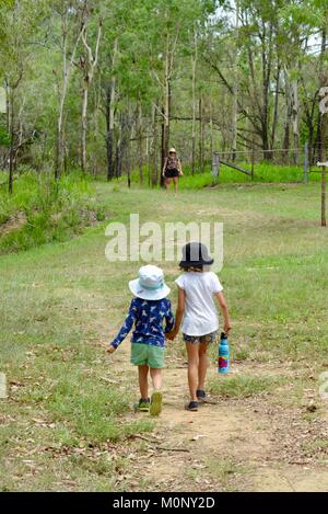 Kinder halten sich an den Händen, während entlang einem Feldweg in einem Feld zwischen einem Wald, Herveys reichen Erbe Teestuben, Queensland, Australien Stockfoto