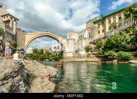 Ein Floß gleitet unter der Alten Brücke in Mostar, Bosnien und Herzegowina auf dem Fluss Neretva mit Touristen auf der Bank und Koski Mehmed Pascha Moschee hinter Stockfoto