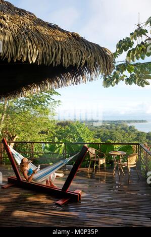 Costa Rica, Halbinsel Osa, junge Frau mit Strohhut in Ihrer Hängematte auf der Terrasse fo der Ecolodge Lapa Rios mit Blick auf den Wald und den Pazifischen Ozean Stockfoto