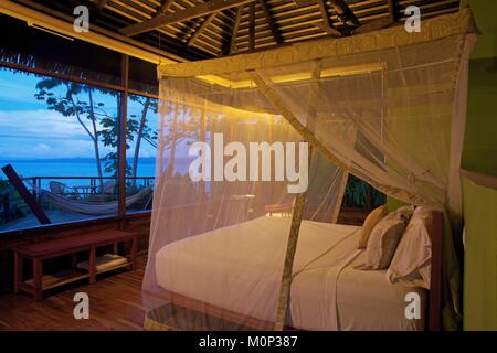 Costa Rica, Halbinsel Osa, Suite mit einem Bett mit einem Netz mit Blick auf eine Terrasse am Meer bei Einbruch der Dunkelheit Öffnen geschützt Stockfoto