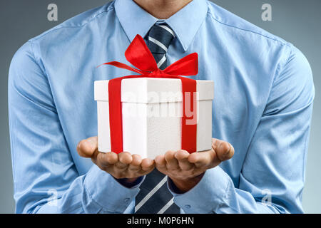 Mann im blauen Hemd mit weißen Geschenkbox mit roter Schleife. Close Up. Business Konzept Stockfoto