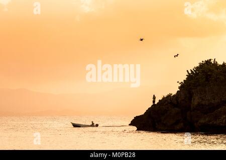 Frankreich, Karibik, Kleine Antillen, Guadeloupe, Grande-Terre, Le Gosier, Sonnenuntergang auf einem Fischerboot und die Küstenlinie überflogen um 2 braune Pelikane (Pelecanus occidentalis) vom Strand von La Créole Beach Hotel Stockfoto