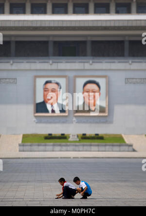 Nordkoreanischen Jungen spielen vor Kim Il Sung und Kim Jong Il riesige Porträts auf Kim Il Sung Platz, Pyongan Provinz, Pyongyang, Nordkorea Stockfoto