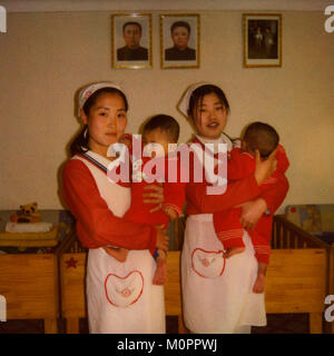 Polaroid von Krankenschwestern und die Pflege von Babys in einem Waisenhaus unter der offiziellen Portraits des Liebe Verantwortliche, Süd-pyongan Provinz, Nampo, Nordkorea Stockfoto