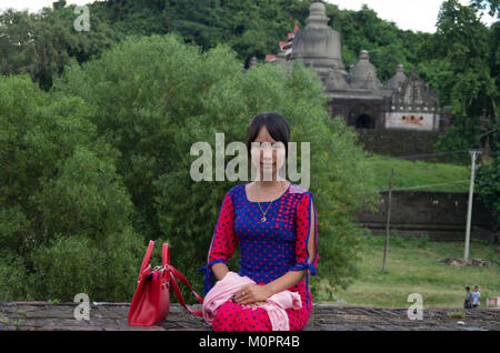 Portrait einer jungen, hübschen Frau mit einem traditionellen Kleid sitzt auf einer Wand vor dem Haupttempel in Mrauk U, Rakhine, Myanmar Stockfoto