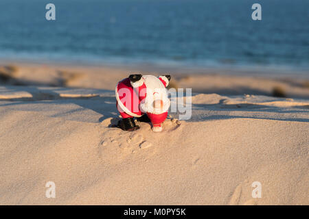 Der Weihnachtsmann spielt Akrobatik an einem sonnigen Strand und verbindet Urlaubsstimmung mit Sommerspaß in einer verspielten und unerwarteten Umgebung am Meer Stockfoto