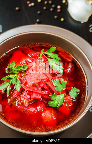 Red borscht Suppe mit Petersilie in brauner Schale Draufsicht, auf Schwarz Tabelle Stockfoto