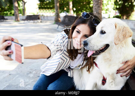 Junge hübsche Mädchen und goldenen Hund ein Selbstporträt mit ihrem Telefon in städtische Umwelt im Sommer. Stockfoto