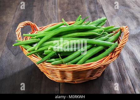 Grüne Bohnen String in Weidenkorb auf einem alten Holz- schwarzen Hintergrund. Ansicht von Oben. Stockfoto