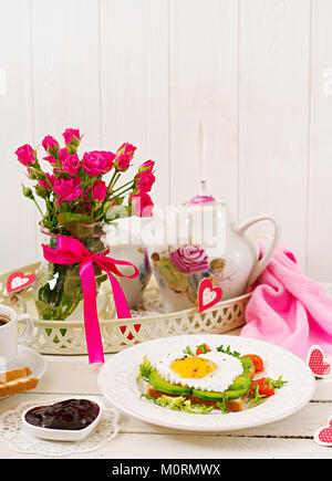 Frühstück am Valentinstag - Sandwich von Spiegelei in Herzform, Avocado und frischem Gemüse. Tasse Kaffee. Englisches Frühstück. Stockfoto