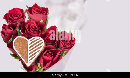 Blumenstrauß aus roten Rosen und süsses Herz für gutes Glück. Blumen zum Valentinstag Hintergrund mit verzierten Lebkuchen. Mutter- oder Frauentag, Geburtstag, Hochzeit. Stockfoto