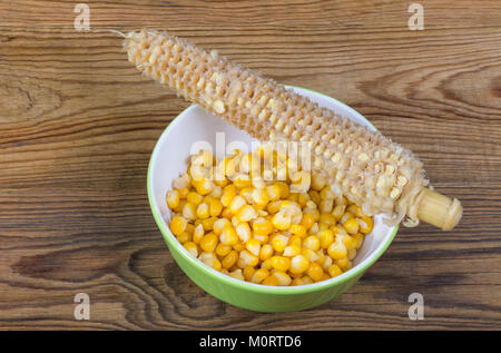 Gekochten Mais und leere Maiskolben. Gelben Maiskörner in runde Schüssel und Zerbissen cob auf einer hölzernen Hintergrund. Stockfoto