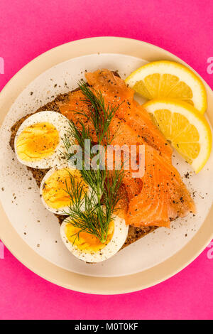 Geräucherter Lachs mit gekochten Eiern offenes Gesicht Sandwich auf Roggenbrot mit Dill gegen einen rosa Hintergrund Stockfoto