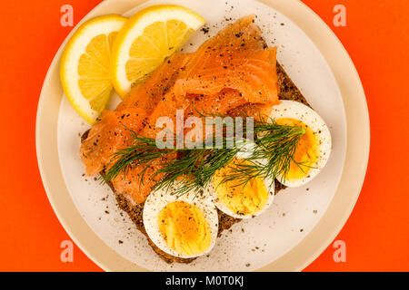 Geräucherter Lachs mit gekochten Eiern offenes Gesicht Sandwich auf Roggenbrot mit Dill gegen einen orangen Hintergrund Stockfoto