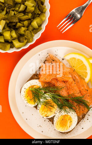 Geräucherter Lachs mit gekochten Eiern offenes Gesicht Sandwich auf Roggenbrot mit Dill gegen einen orangen Hintergrund Stockfoto