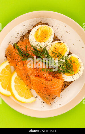 Geräucherter Lachs mit gekochten Eiern offenes Gesicht Sandwich auf Roggenbrot mit Dill vor einem grünen Hintergrund Stockfoto