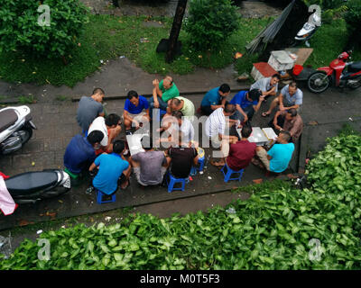 Foto mit einer Gruppe von Kartenspielern in einem Park am Straßenrand in der Nähe von Hanoi, die einen Moment des täglichen Lebens in Vietnam festhalten. Stockfoto
