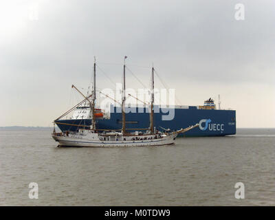 Ein Foto, das sowohl ein Carrier-Schiff als auch ein traditionelles Segelschiff zeigt und den Kontrast zwischen moderner Transporttechnik und klassischer maritimer Handwerkskunst unterstreicht. Das Bild erfasst beide Gefäßtypen in einem Bild. Stockfoto