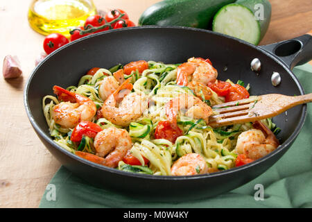 Zucchini Spaghetti sauteed mit Cherry Tomaten und Garnelen in einer Pfanne auf einem rustikalen Holztisch. Nahaufnahme Stockfoto