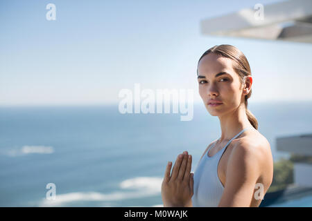 Portrait heitere Frau Yoga mit Händen am Herzen Zentrum auf der sonnigen Terrasse mit Blick auf den Ozean Stockfoto