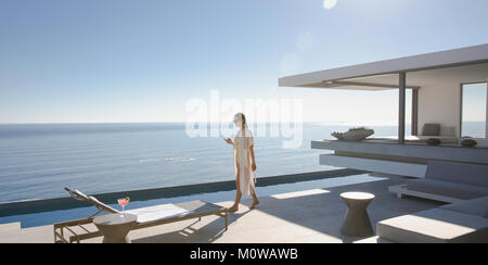 Frau gehen auf das sonnige, moderne, luxuriöse Home Showcase äußere Terrasse mit Meerblick Stockfoto