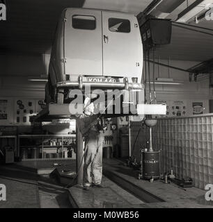1950er Jahre, historische Bild eines männlichen garage Mechaniker in Overalls unter einem kleinen Motor Fahrzeug arbeiten und mit einem langen ölpresse die hintere Antriebswelle, England, UK zu schmieren. Stockfoto