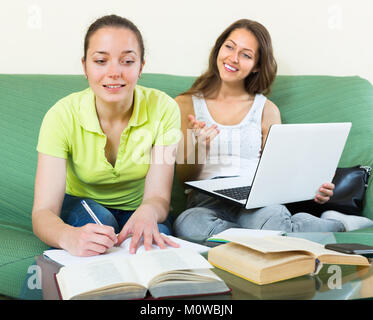 Zwei lächelnde Freundinnen sitzen auf einem Sofa und Hausaufgaben zu Hause Stockfoto