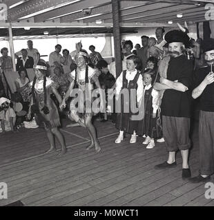 1950, historische, Eltern sehen ihre Kinder tragen verschiedene Länder native Kostüme in einem fancy dress Wettbewerb auf dem Deck an Bord eines Dampfschiffes Union-Castle vorangegangen für die Kap in Südafrika. Stockfoto