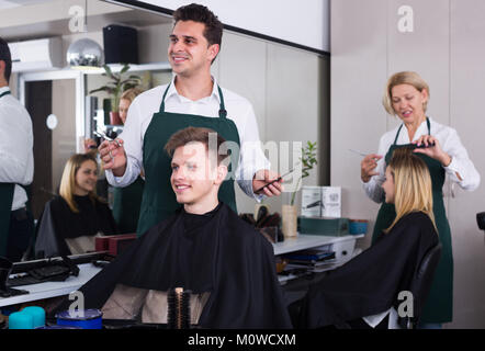 Positive männliche hairstyler mit Teenager im Stuhl von Salon Stockfoto