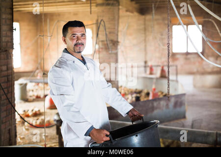 Ältere Arbeitnehmer im weißen Mantel holding Plastikeimer auf Geflügel Farm Stockfoto