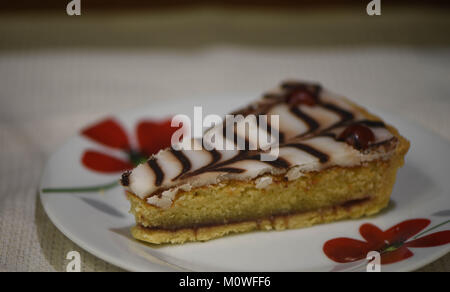 Nahaufnahme makro Food Fotografie aus einer Scheibe hausgemachten Bakewell tart oder Kuchen auf einem roten Blumen Platte mit Schokolade Muster Vereisung und Kirschen Stockfoto