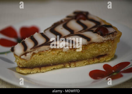 Nahaufnahme makro Food Fotografie aus einer Scheibe hausgemachten Bakewell tart oder Kuchen auf einem roten Blumen Platte mit Schokolade Muster Vereisung und Kirschen Stockfoto